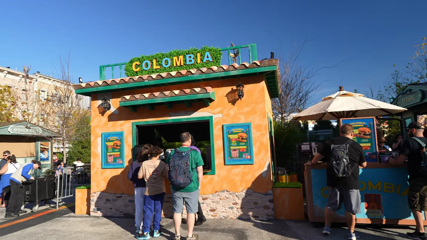 Universal Mardi Gras 2027 Ends a Week Earlier Than in 2026 2 A colorful Colombia food booth at the Mardi Gras festival, with guests reading the menu.