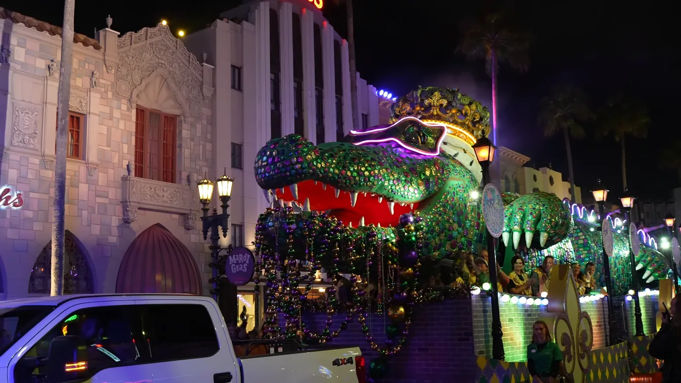 Universal Mardi Gras 2027 Ends a Week Earlier Than in 2026 1 A brightly lit green alligator-themed Mardi Gras parade float beside Universal Orlando buildings at night.