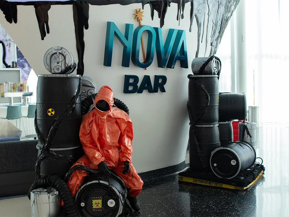 HHN 2026 Food, Shows and Merchandise: What to Prioritize 6 Orange hazmat-suit mannequin and black barrels beneath the Nova Bar sign