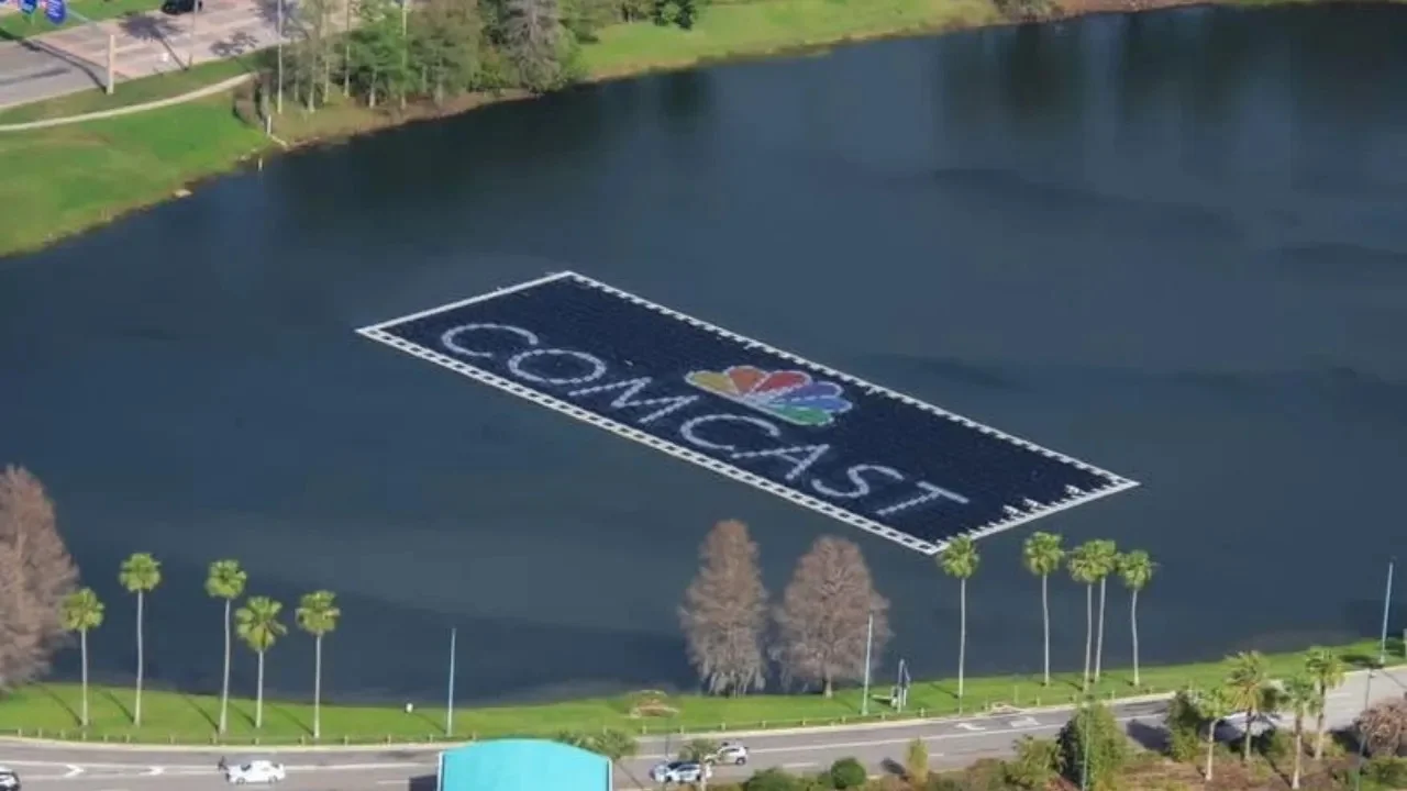 Epic Universe Uses Floating Solar Panels to Charge Electric Buses 3 Aerial view of a floating solar array displaying the Comcast logo on a pond